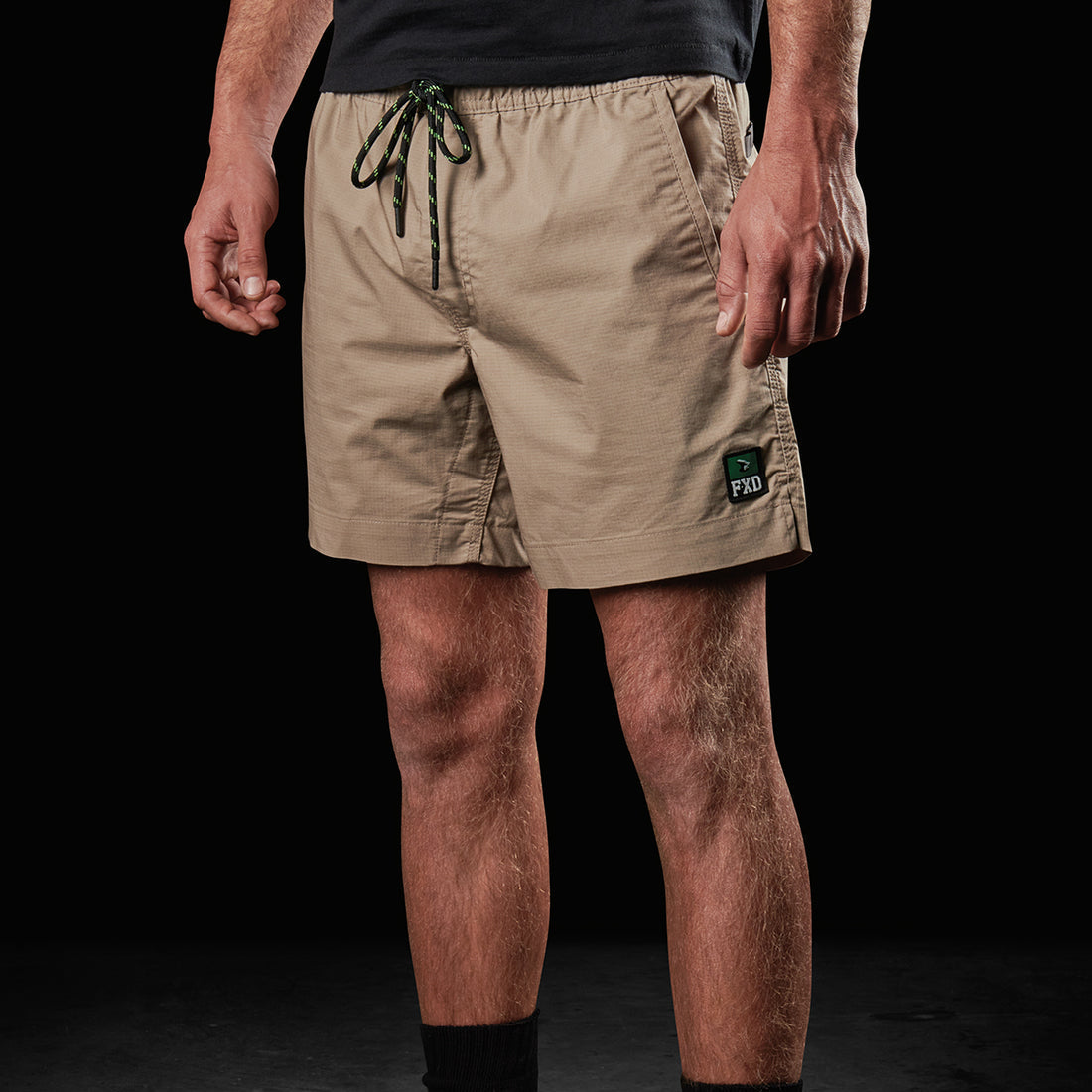 Person wearing beige shorts and brown boots on a black background